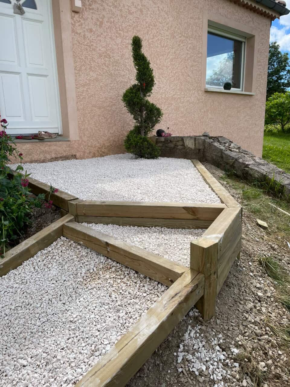 Aménagement d'entrée en gravier blanc avec bordures bois et topiaire